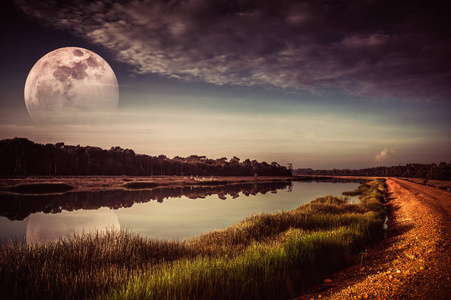 美丽的天空与云和褪色的一半超月以上的树木剪影在河畔。宁静的自然背景。晚上户外。用我的相机拍摄的月亮