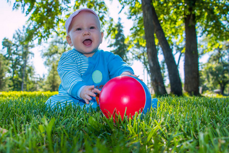 婴儿坐在城市公园的柔软的草地上, 他的彩色球