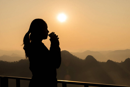 妇女在橙色背景下喝茶的黑暗剪影与山