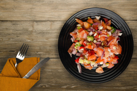 纯素食物蔬菜沙拉 胡椒西红柿洋葱花椰菜 放在盘子里。木制背景下的纯素沙拉