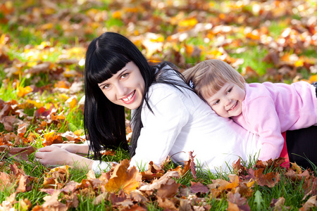 美丽的年轻母亲和她的女儿躺在秋天树叶上