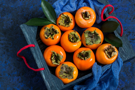成熟的柿子在盒与蓝色纱布餐巾在蓝色纹理背景。柿子是维生素 C碘铁钾和镁的来源。有助于预防心血管疾病