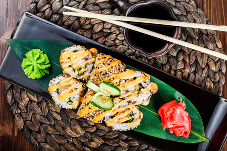 寿司卷上放有虾天妇罗黄瓜洋葱鳄梨和芝麻上的黑石上的竹垫, 选择性对焦。日本料理