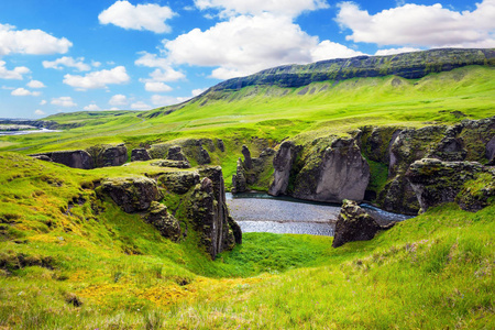 在冰岛醒目的峡谷。冰岛苔原在7月。北方旅游活动的概念。垂直的巨大岩石环绕溪流与冰川水