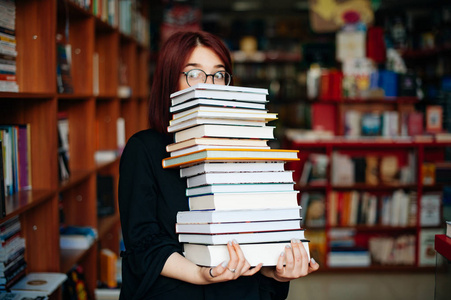 有眼镜的书女孩在图书馆里捧着一堆书