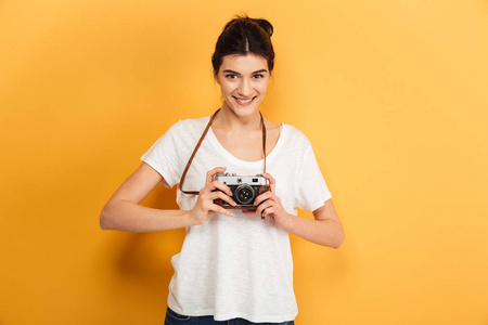 形象的情绪快乐年轻漂亮的女子摄影师站在黄色背景持有摄像头隔离