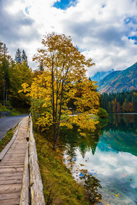 Fusine 湖周围的路, 用木制扶手围起来。水面的光滑反映了多云的天空。文化生态旅游理念