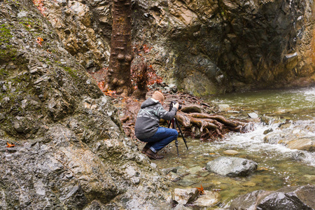 年轻的摄影师与背包制作照片的瀑布和岩石与相机。地中海