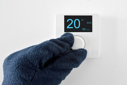 一只手用手套调整恒温器在家里的数字温度