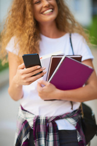 女学生在校园漫步时使用智能手机和手持书本