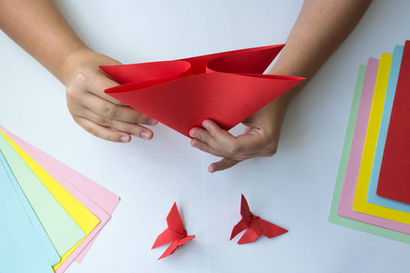 儿童的手做折纸蝴蝶从彩色纸在白色背景。折纸蝴蝶课