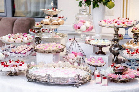 美味的婚宴糖果酒吧甜点桌上满是蛋糕和糖果, 还有一个花花瓶和绣球。奢华生活