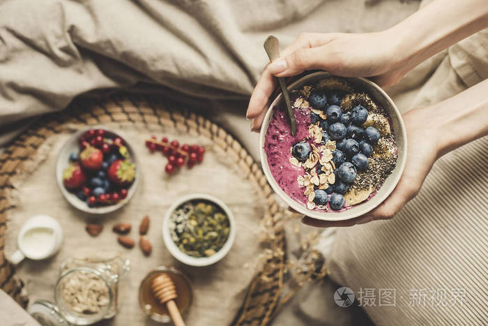 健康早餐在床上.手捧着美味的冰鲜碗, 蓝莓, 燕麦和嘉籽