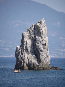 一个陡峭的小岩石在蓝色海的中央在距离一个大度假镇的背景下