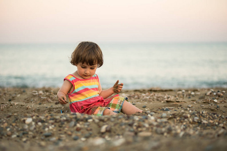 可爱的蹒跚学步婴儿在鹅卵石海滩上玩
