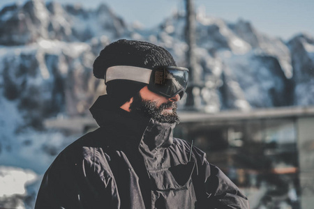 肖像的胡子英俊的 snowboarded 在太阳镜面具, 在滑雪胜地的背景山和蓝天。背景模糊。水平. 彩色掩码