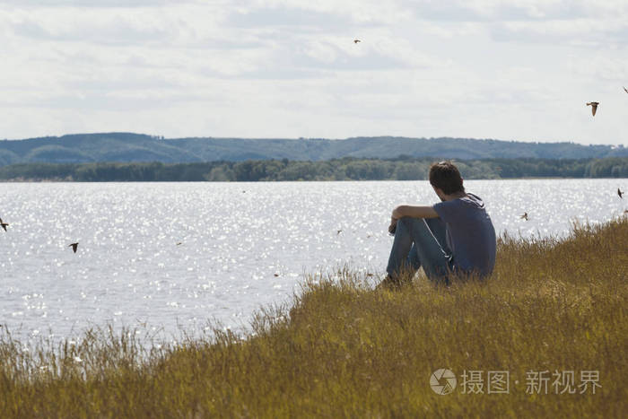 年轻的悲哀的人坐在山上看着远处飞过河边照片-正版商用图片05ejr9-摄