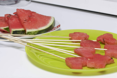 西瓜的果肉是用邮票切碎的。它们被赋予不同的形式。串在一起野餐。盘子旁边是西瓜片