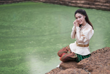 在泰国传统礼服在池塘附近的愉快的美丽的妇女