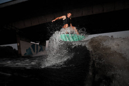 愉快活跃和年轻 wakesurfer 骑马在河波浪对桥梁在夏天晚上