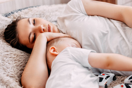 美丽的年轻妈妈和她可爱的小宝宝，睡在床上在家里的侧视图