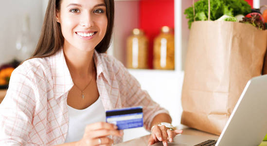 微笑的妇女在线购物使用平板电脑和信用卡在厨房。微笑的妇女