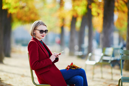 优雅的巴黎妇女使用她的手机在公园的一个灿烂的阳光明媚的秋天天