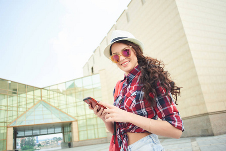 可爱的女人游客在夏天的衣服与智能手机走在街上