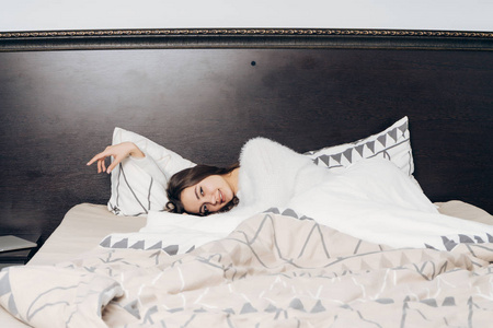 一个穿着白色睡衣的甜美昏昏欲睡的女孩躺在床上清晨, 不想起床
