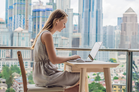 年轻女子正在阳台上的笔记本电脑上俯瞰摩天大楼。自由职业者, 远程工作, 在家工作