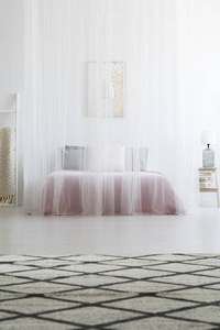花纹地毯在 scandi 卧室内部与白色面纱在床之上。真实照片