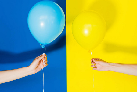 女性在蓝色和黄色背景下使用气球的裁剪视图