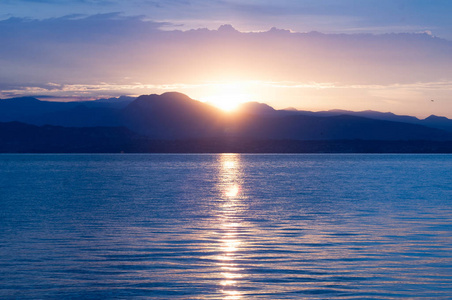 湖上日出。清晨的全景。山在剪影和上升的耀眼的太阳的光芒。在意大利的爱尔兰湖日出