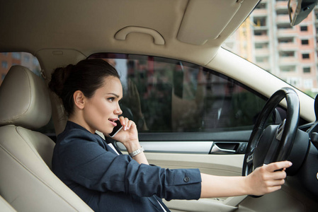 驾驶汽车时使用智能手机的迷人女性侧面视图