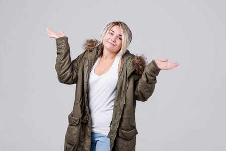 一个穿着秋季保暖夹克的年轻女孩在灰色背景上收听无线耳机上的音乐