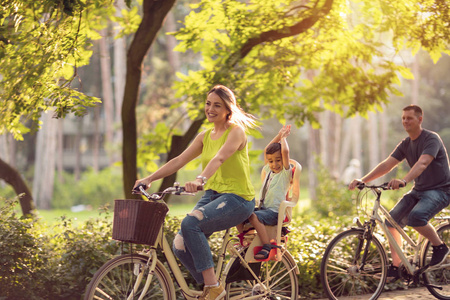 快乐的家庭骑自行车户外和微笑小男孩骑自行车与母亲和父亲