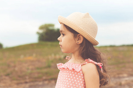 美丽的小女孩, 长头发的草帽, 在日落的夏季田野看着远离