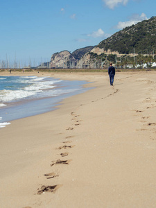 人漫步在海滩上的 Castelldefels 和标志的步骤在沙子