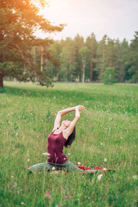 在森林附近的田野上做瑜伽的年轻漂亮女子
