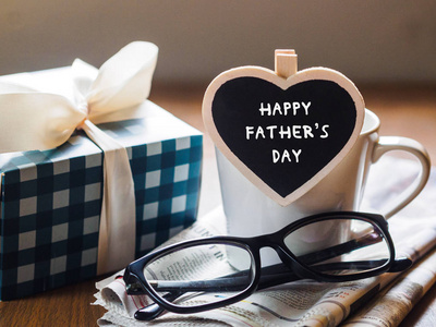 快乐的父亲日概念。咖啡杯配礼品盒, 心贴标签与快乐父亲节文本和报纸, 眼镜在木桌背景上