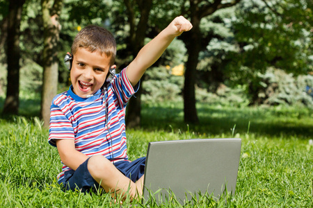 男孩在公园中使用他的笔记本电脑户外
