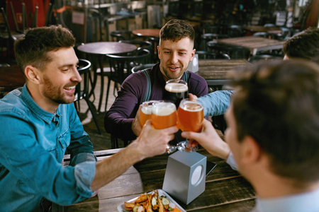 在酒吧喝啤酒的男人朋友们在酒吧里用酒精饮料干杯。高分辨率