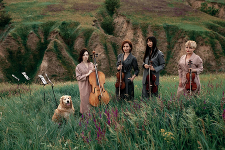 女性音乐四重奏与三小提琴和一大提琴准备演奏在开花的草甸反对在风景如画的风景旁边狗的背景