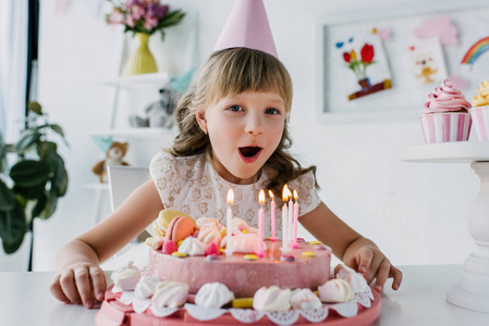 微笑的孩子在锥体吹出蜡烛从生日蛋糕