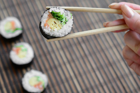 一只手拿着筷子在竹稻草 serwing 垫的背景上放上寿司卷。传统亚洲食品