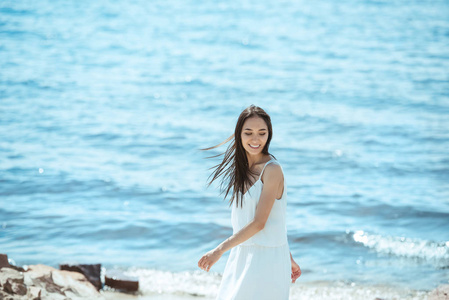 微笑的亚洲妇女在白色礼服站立在海在白天