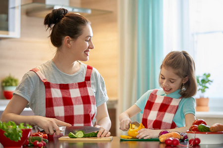 健康的食物在家里。幸福的家庭在厨房里。母亲和孩子的女儿正在准备蔬菜