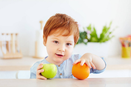 可爱的红发学步婴儿抱着新鲜的苹果和橙色的水果