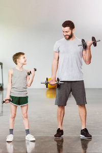可爱的小男孩训练与哑铃一起与父亲在健身中心