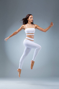 迷人的兴奋健身女孩, 芭蕾舞演员在运动装束跳的喜悦孤立的灰色背景